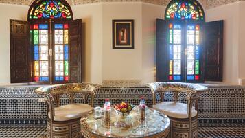A room with two ornate wooden doors with stained glass windows, a patterned floor, and a round table with chairs and a fruit bowl.