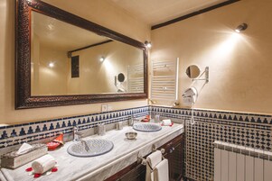 Un baño con un espejo grande, dos lavamanos, un perchero para toallas y un secador de pelo.