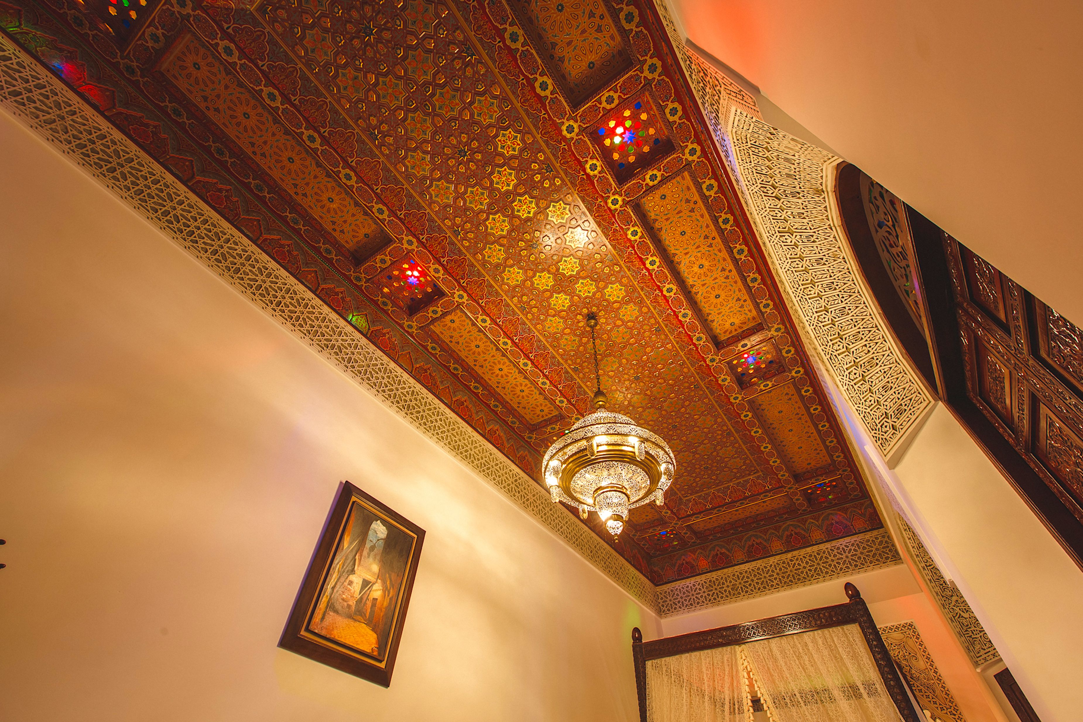 Quarto com padrões ornamentais no teto, um candelabro e um quadro na parede.