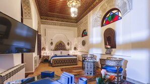 A room with a bed, a TV, a small table, and a chair. - Riad Fes Maya (Fes)