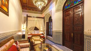 A traditional Moroccan room with a sofa set, a glass coffee table, and ornate wooden doors. - Riad Fes Maya (Fes)