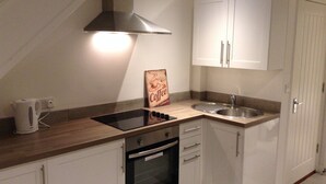 A compact kitchen with white cabinets, a stainless steel sink, a built-in oven, and a coffee-themed sign. - Central Windsor Apartments (Windsor)