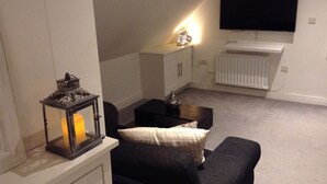 A living room with a sofa, a TV mounted on the wall, a radiator, and a decorative lamp. - Central Windsor Apartments (Windsor)
