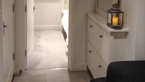 A narrow hallway with a door leading to a bedroom. There is a dresser with a mirror and a candle on top. - Central Windsor Apartments (Windsor)