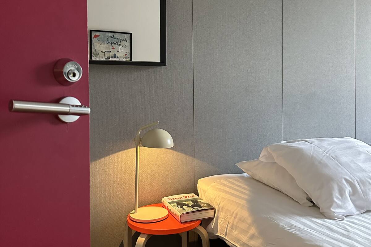Ein Hotelzimmer mit Bett, Nachttisch mit Lampe, Stuhl und Tür.