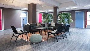 Un área de lounge moderna con una mesa redonda, sillas negras y un pouf gris.