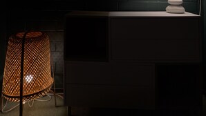 Una habitación moderna con pared de ladrillo oscuro, una lámpara blanca sobre una mesa de madera y una silla de mimbre.
