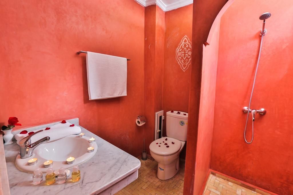 Uma casa de banho com uma sanita, chuveiro e lavatório branco.