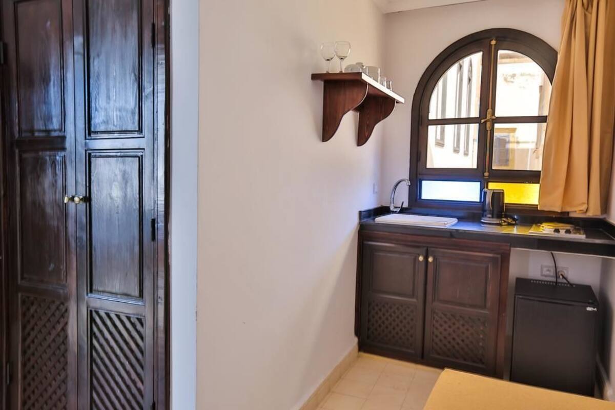 A compact kitchen with a built-in sink, a small refrigerator, and a window with a view of the street.