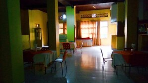 A dining area with tables and chairs, a kitchen area with a stove, and a window with curtains. - Eminence Hotel (Kigali)