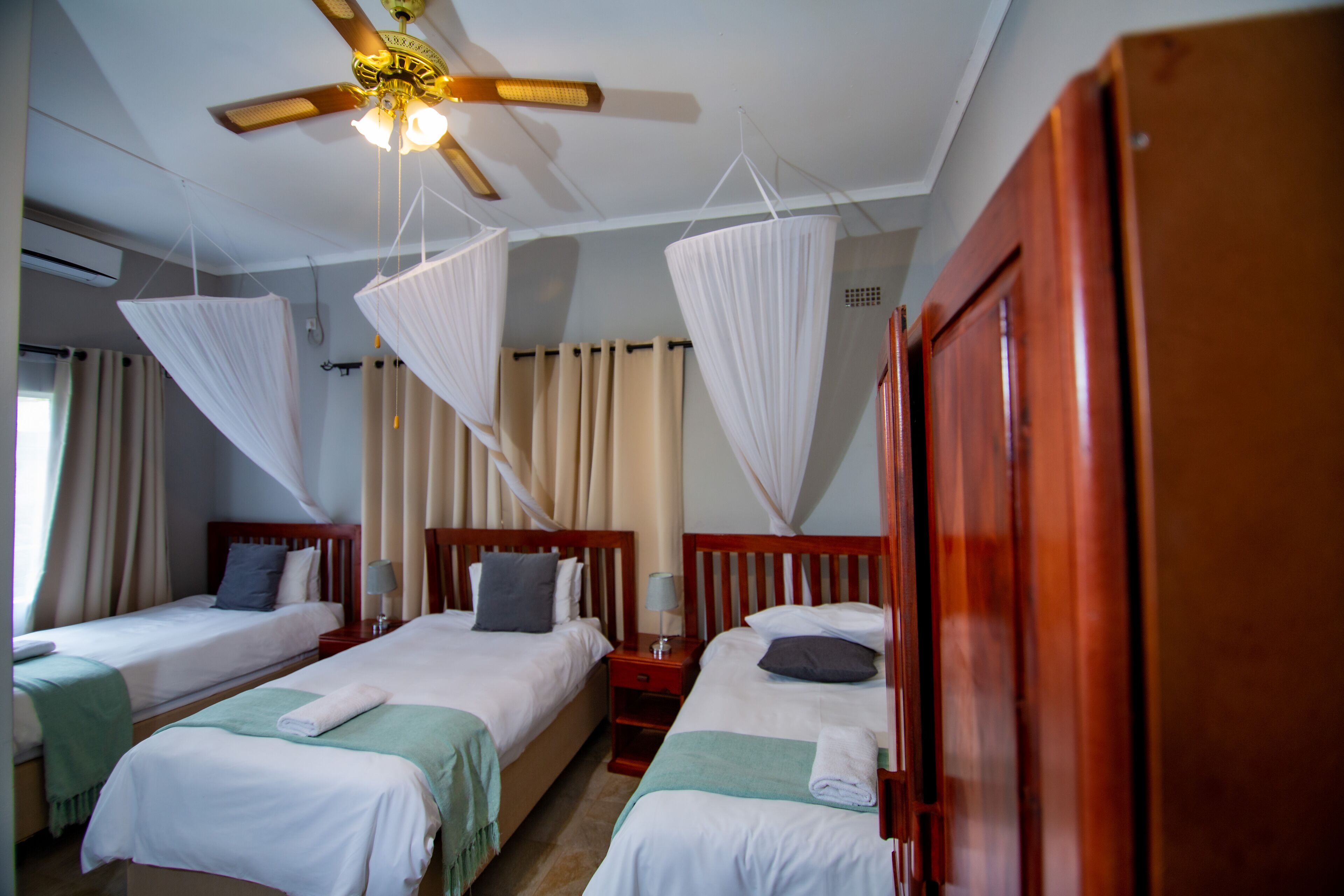 A hotel room with three single beds, a ceiling fan, and mosquito nets.