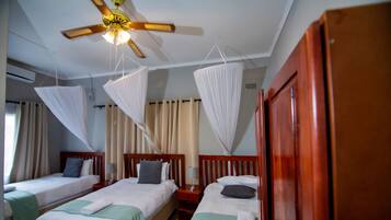 A hotel room with three single beds, a ceiling fan, and mosquito nets.