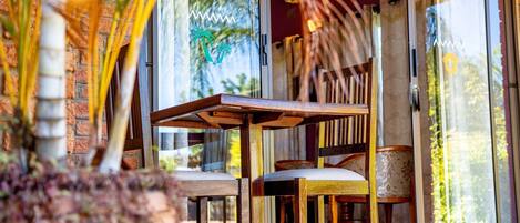 A wooden table and chairs outside a building with glass doors, a brick wall, and a palm tree in the background.