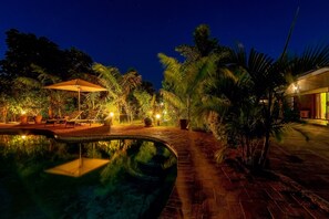 A nighttime pool area with a pathway, lounge chairs, and a canopy. - Dzimbahwe Guest Lodge (Victoria Falls)