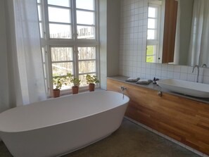 A modern bathroom with a freestanding bathtub, a wooden vanity with a sink, and a large window with potted plants.
