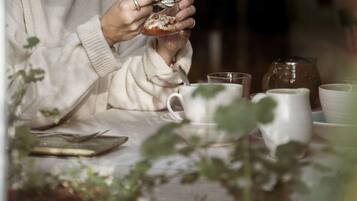 A person holding a glass with a dessert, seated at a table with various cups and a teapot.
