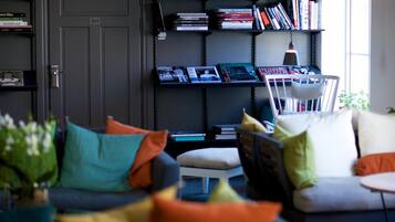 A modern living room with a grey sofa, colorful cushions, a white chair, and a bookshelf filled with books.