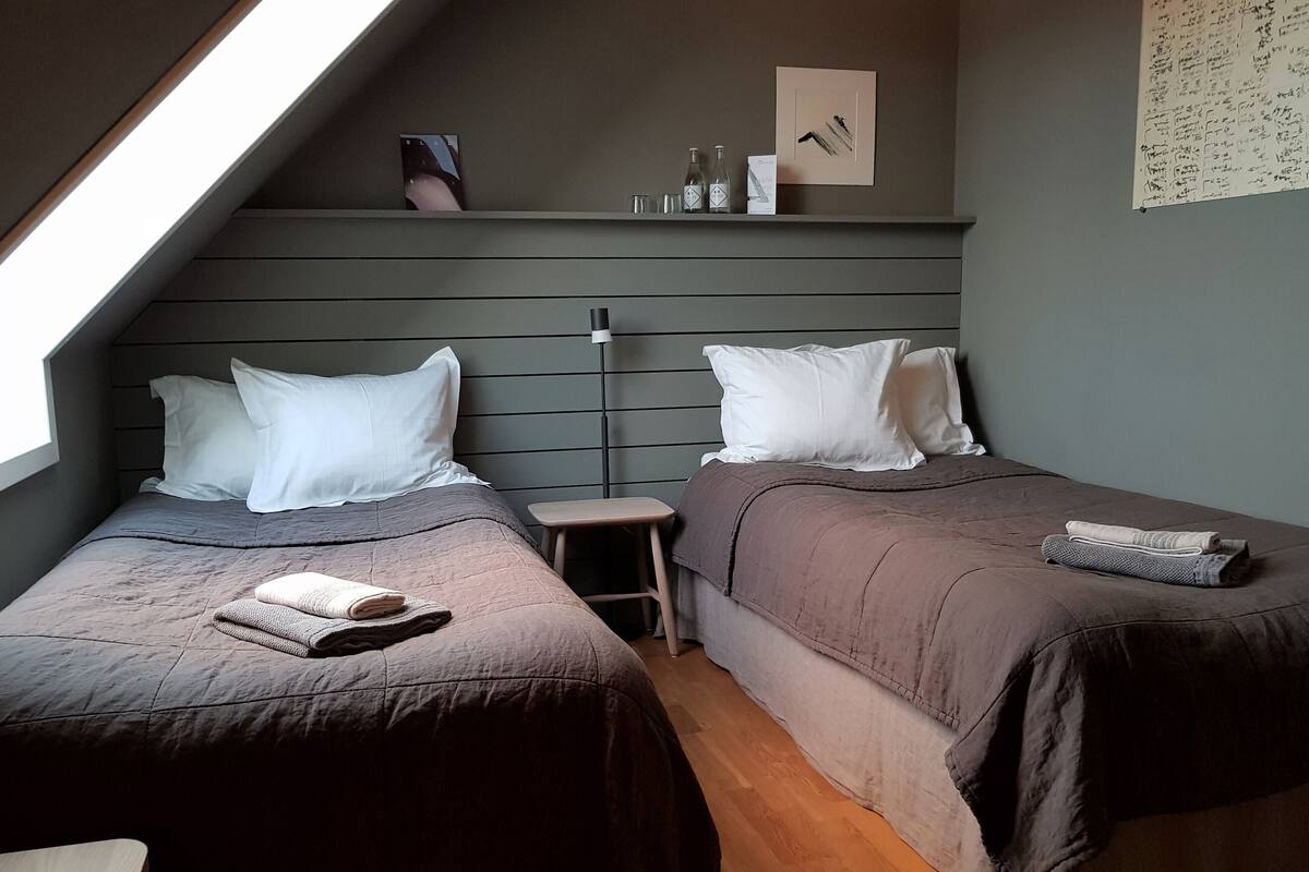A bedroom with two beds, a small stool, a nightstand, and a shelf with items.