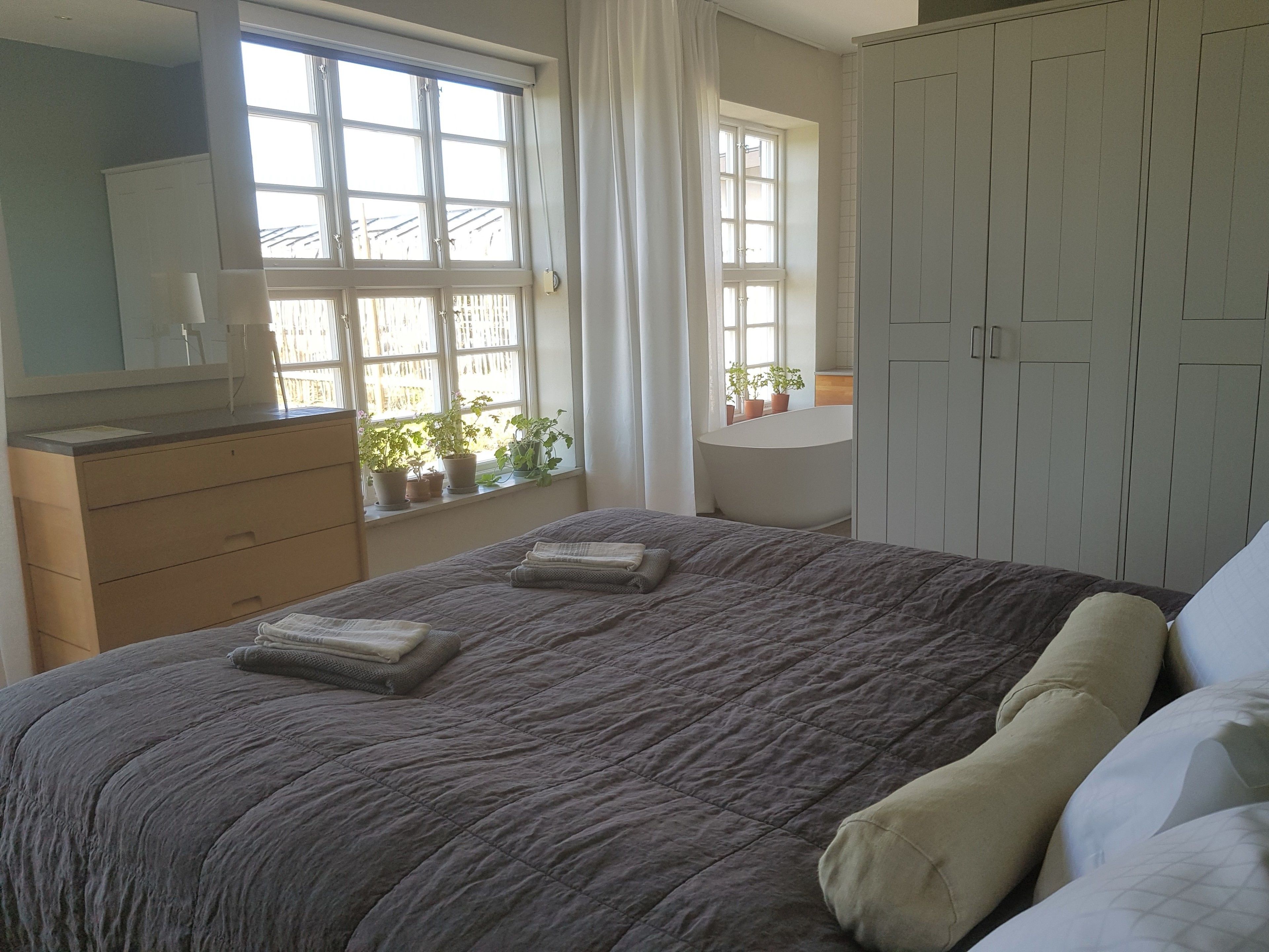 Een slaapkamer met een groot bed, een dressoir, een raam met gordijnen en een kledingkast.