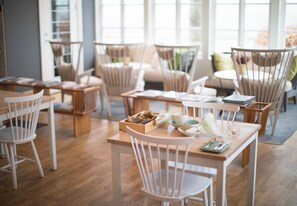 A cozy dining area with wooden tables and white chairs, featuring a menu and a candle on one table.