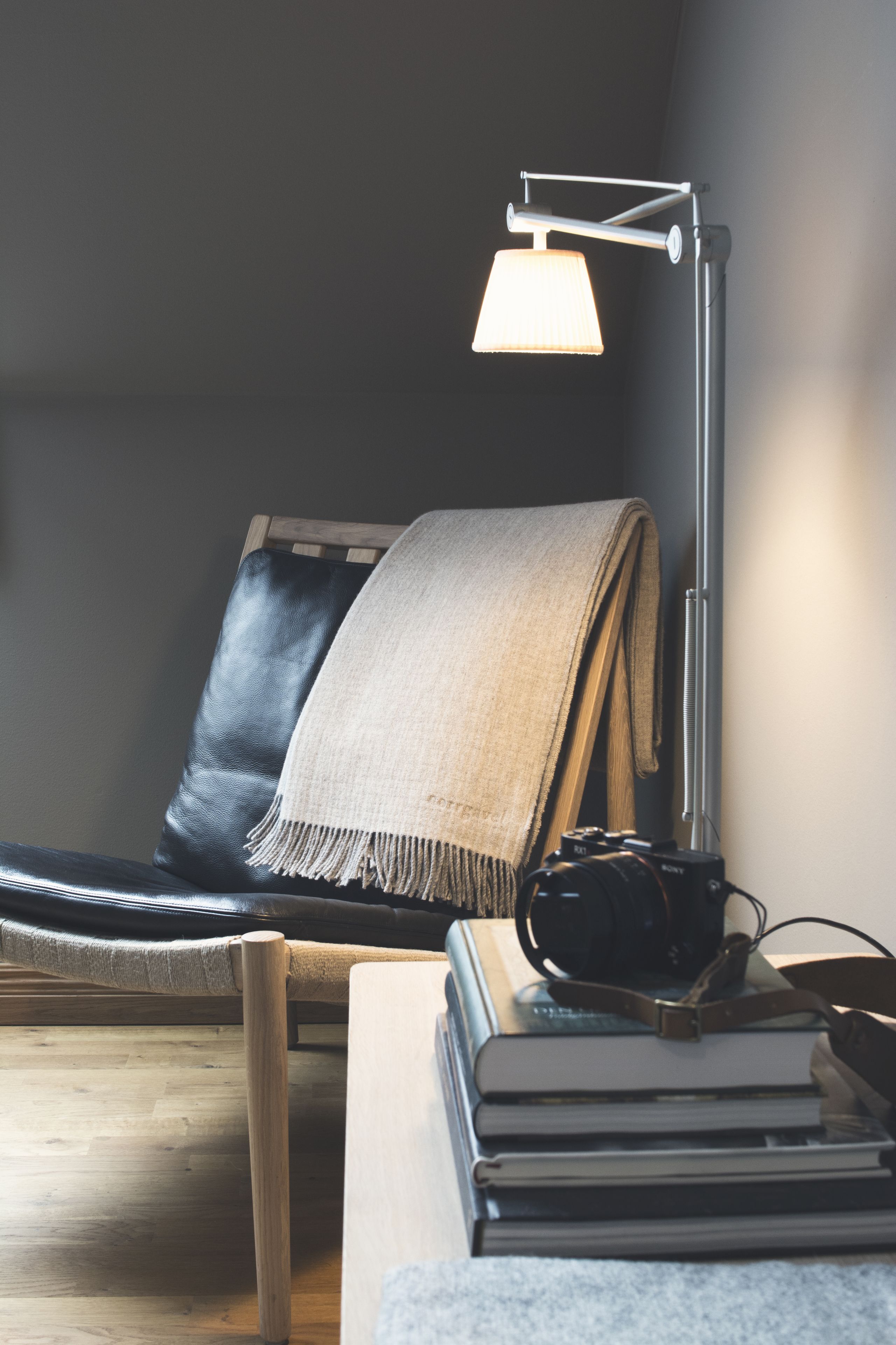 A room with a black leather chair, a beige throw blanket, a desk with a lamp, and a stack of books.