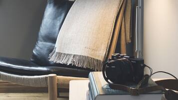 A room with a black leather chair, a beige throw blanket, a desk with a lamp, and a stack of books.