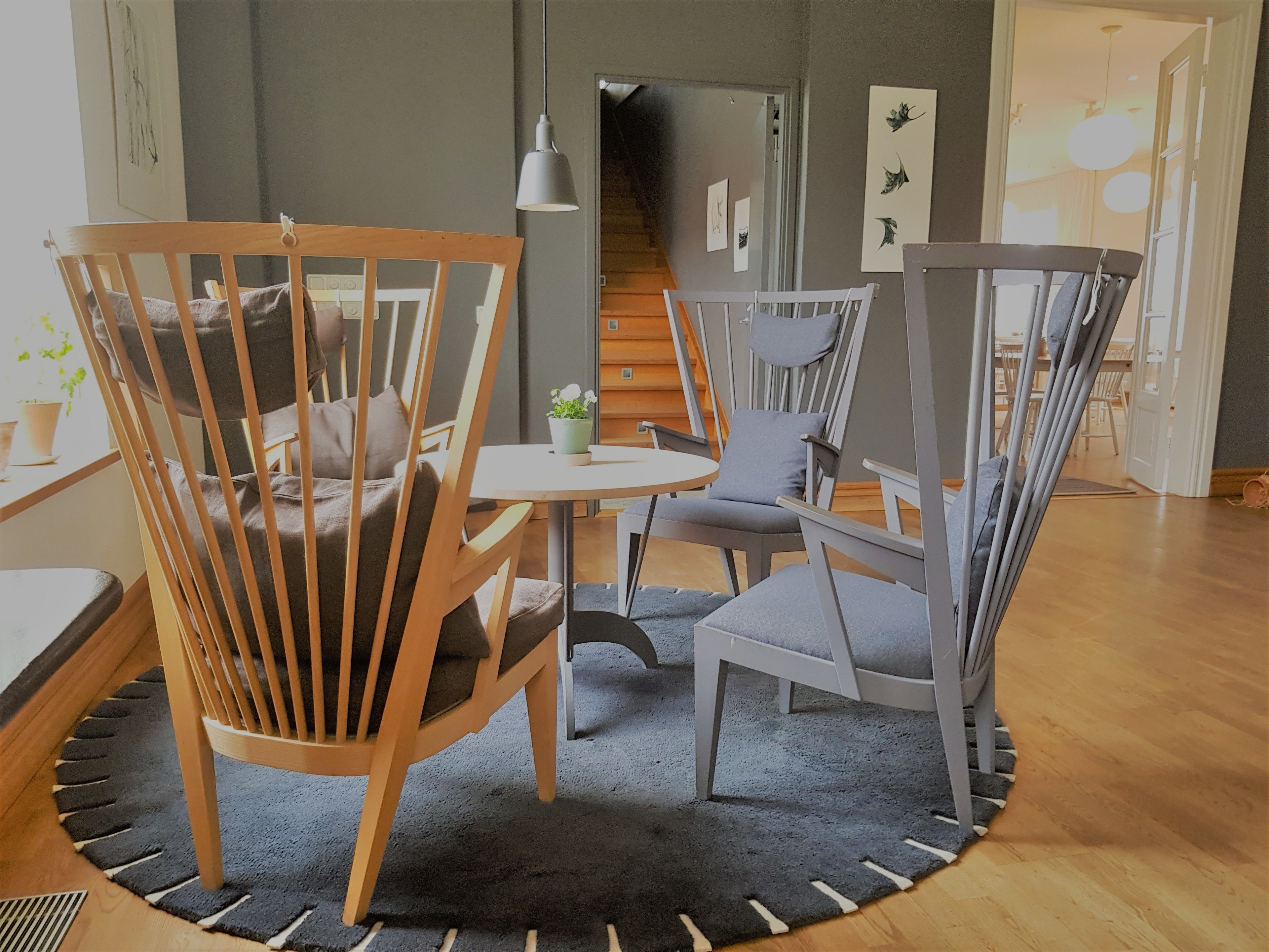 A modern living room with a round table, two wooden chairs, and a grey upholstered chair.