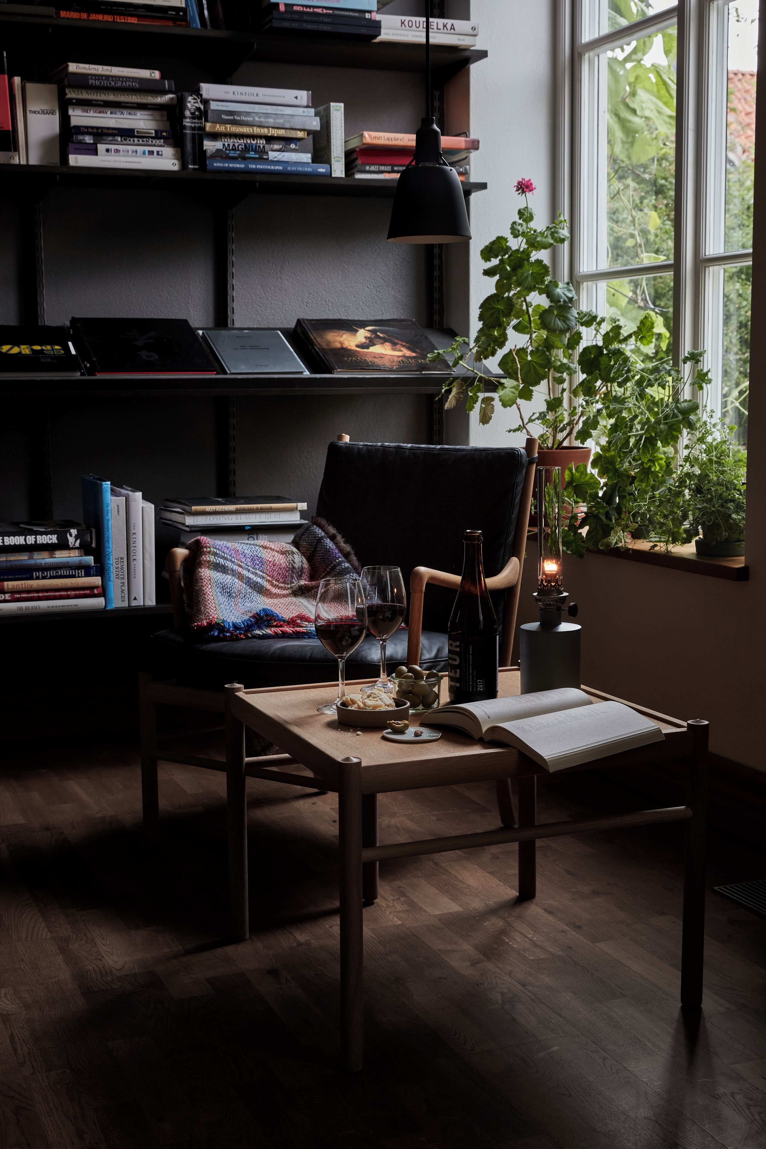 Un rincón acogedor para leer, con un sillón, una mesa y una estantería llena de libros.
