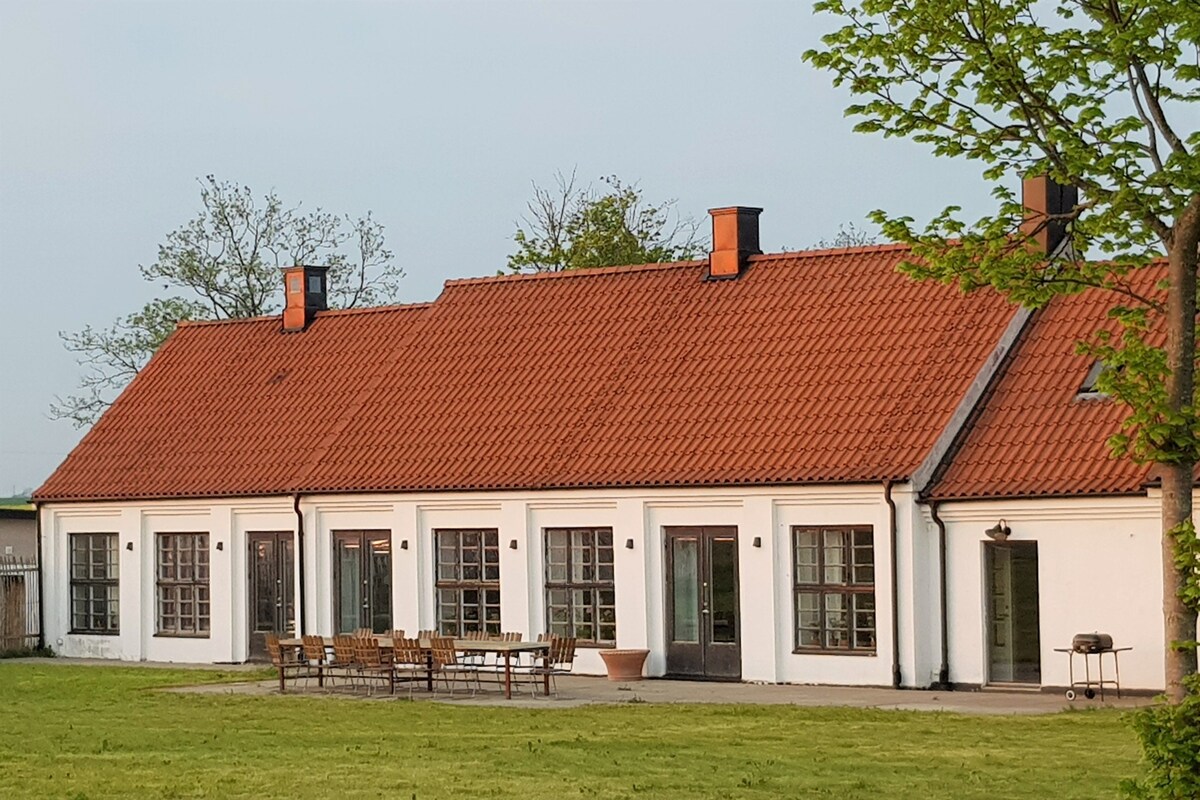 A white building with a red-tiled roof, multiple windows, and a grassy lawn.