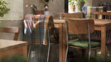 A dining area with wooden tables and chairs, a potted plant, and a window with natural light.