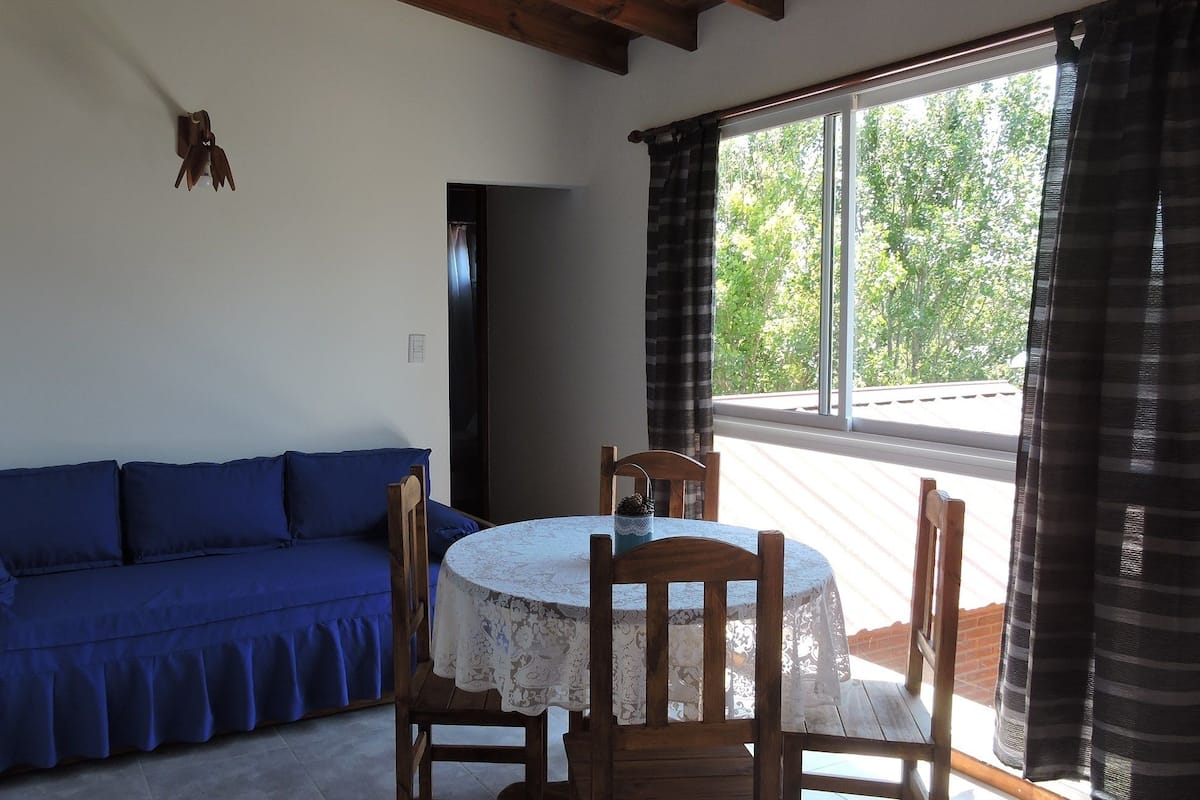A room with a blue sofa, a round table with a lace tablecloth, and a TV mounted on the wall.