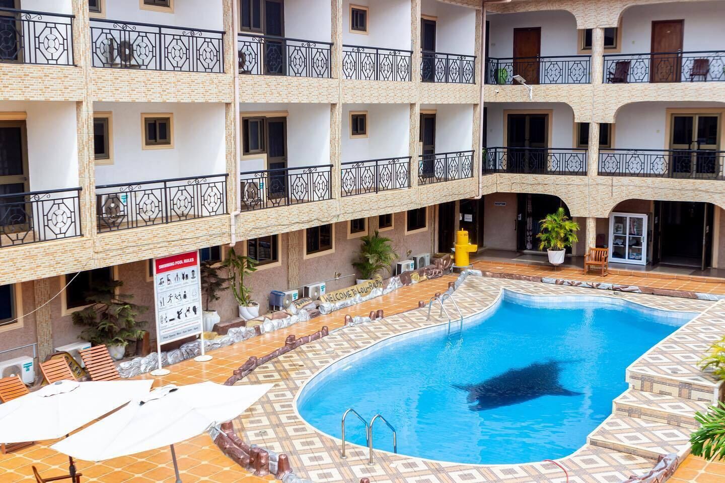 A multi-story building with a central swimming pool, balconies with metal railings, and outdoor seating areas.