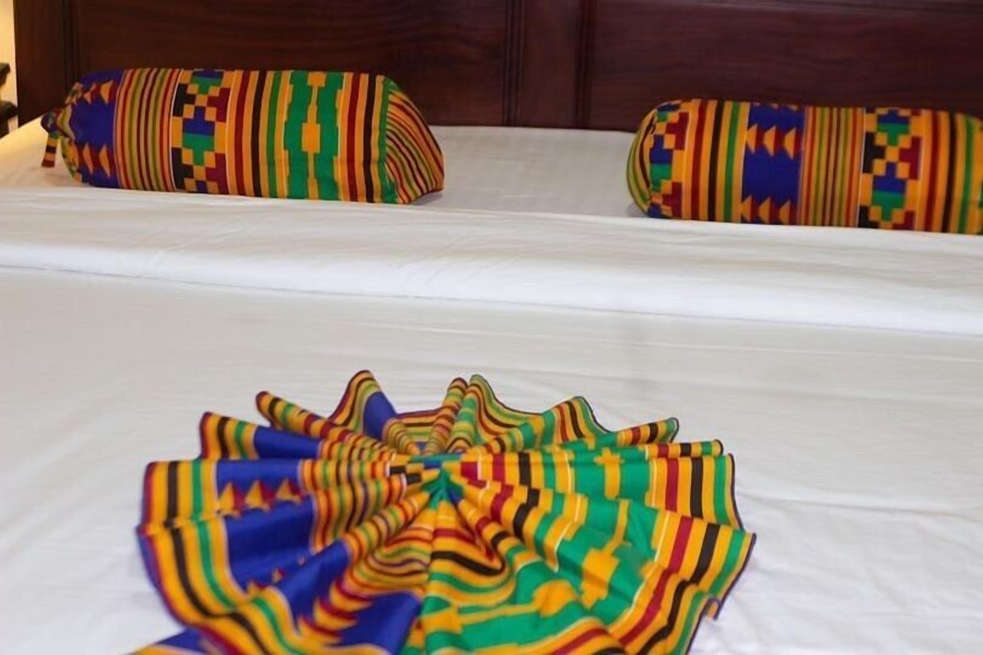 A bed with a white sheet and two pillows with colorful geometric patterns.