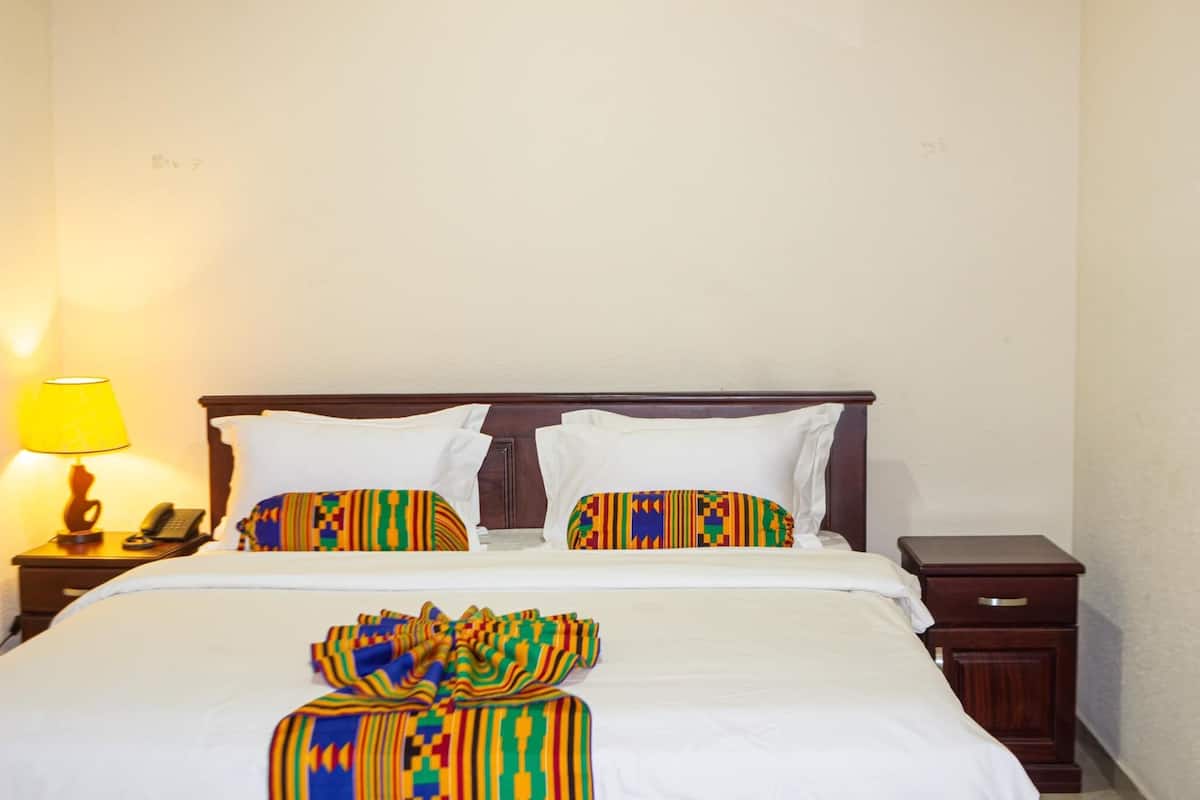 A hotel room with a bed, two pillows, a bedside table with a lamp, and a nightstand with a phone.