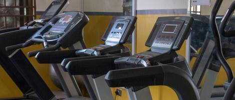 Una fila de bicicletas estáticas en un gimnasio con pared amarilla y gris.
