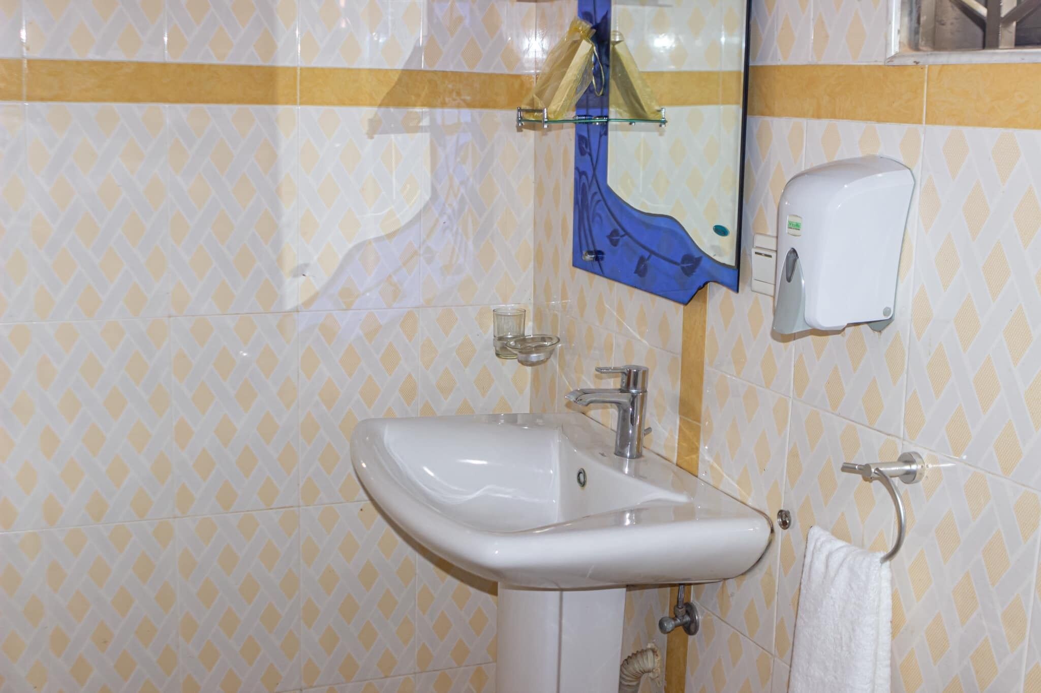Un baño con lavamanos blanco, un espejo, toallero y dispensador de jabón.