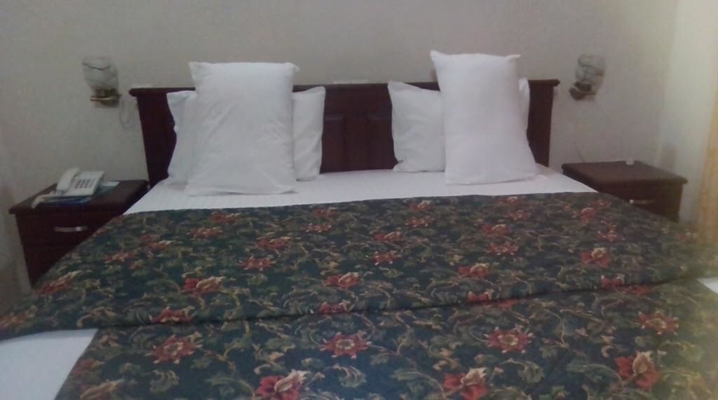 A bed with a floral bedspread, two white pillows, and a wooden headboard.