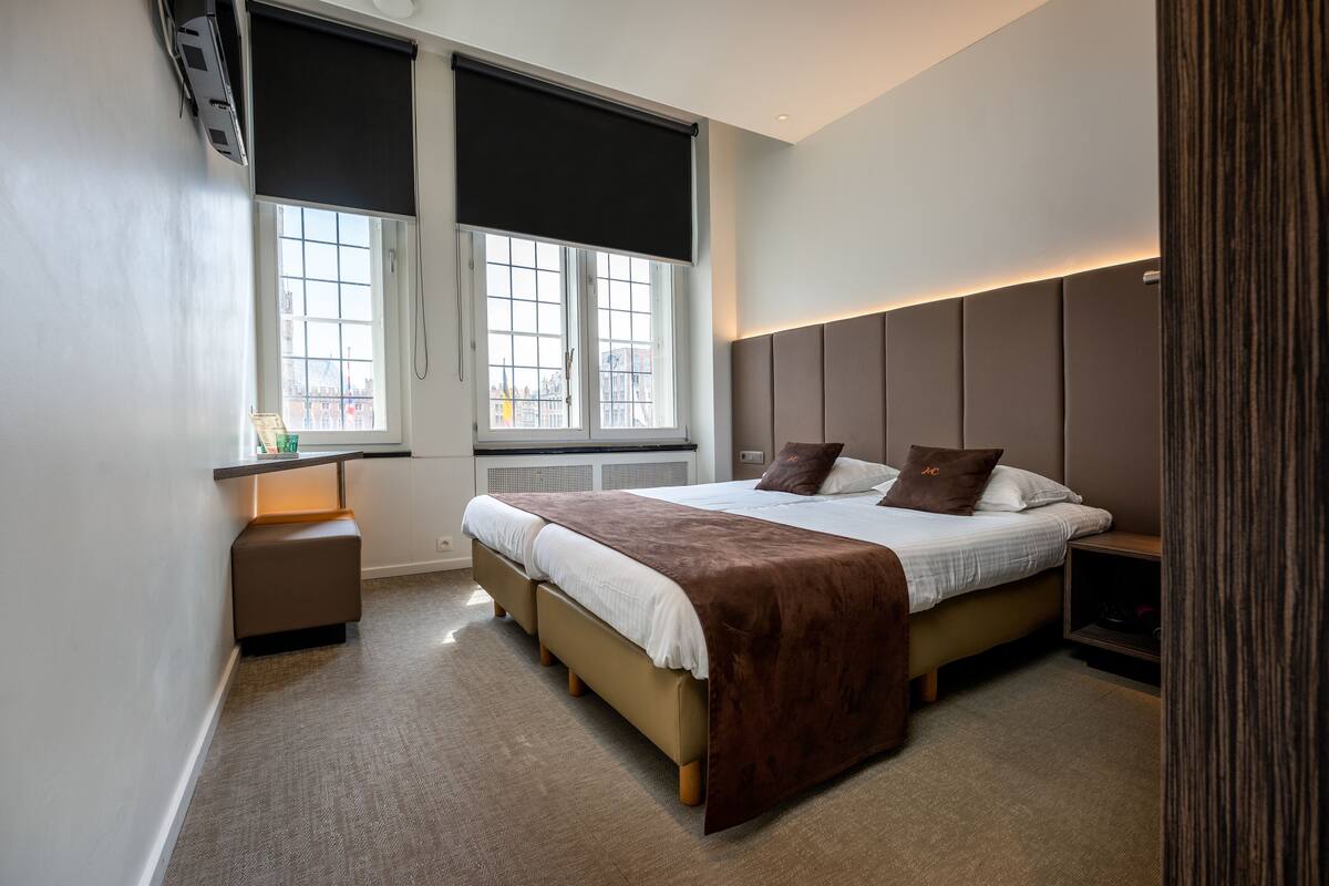 A modern bedroom with a large bed, a bedside table, a bench, and a window with a view of the city.