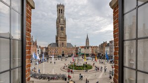 Una plaza histórica con una imponente torre del reloj, rodeada de edificios tradicionales y una fuente en el centro.