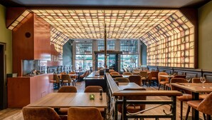 Un restaurante espacioso con techos altos, ventanas amplias y diferentes opciones de asientos, incluyendo mesas y sillas.