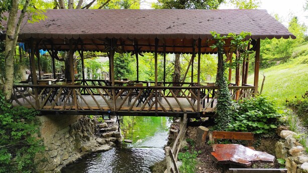 A wooden bridge over a stream with a rustic pavilion on the right. - Kure Dag Evi (Ulus)