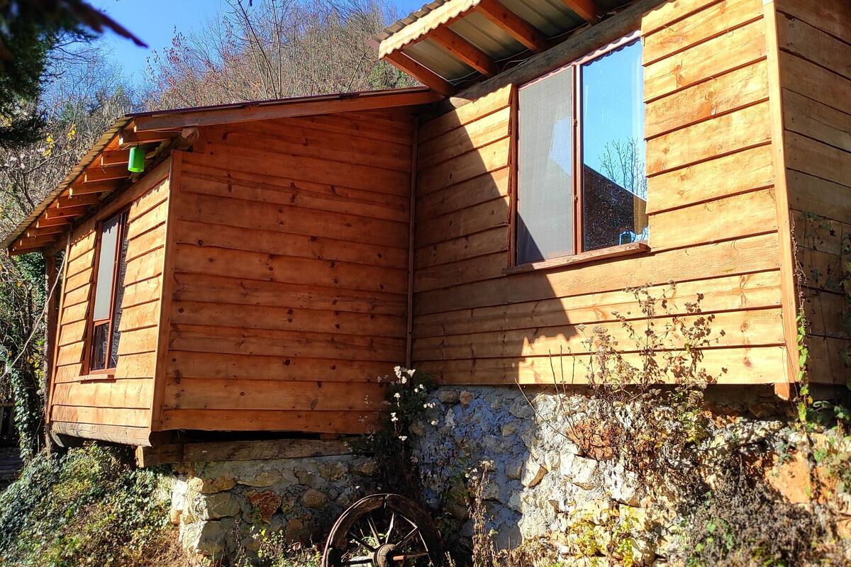 A wooden cabin with a stone foundation, a window, and a door.