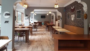 A restaurant with a long wooden table and chairs, a brick wall with framed pictures, and a ceiling fan. - Kure Dag Evi (Ulus)