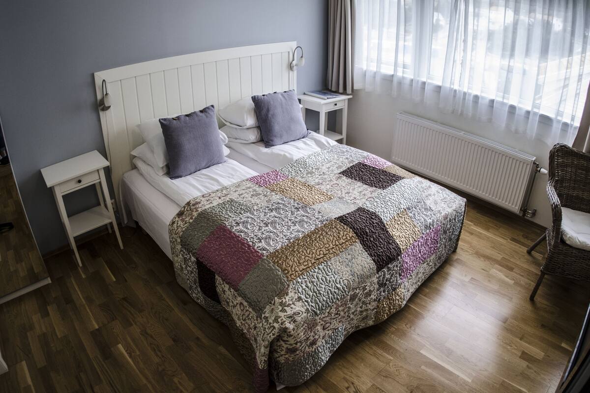 Un letto rifatto con cura, con una coperta a motivi decorativi, una testiera bianca e due comodini con lampade.