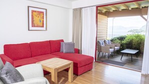 A red sectional sofa with a wooden coffee table, a framed picture on the wall, and a view of the outdoors through a sliding glass door. - Lavik Fjord Hotell (Hoyanger)