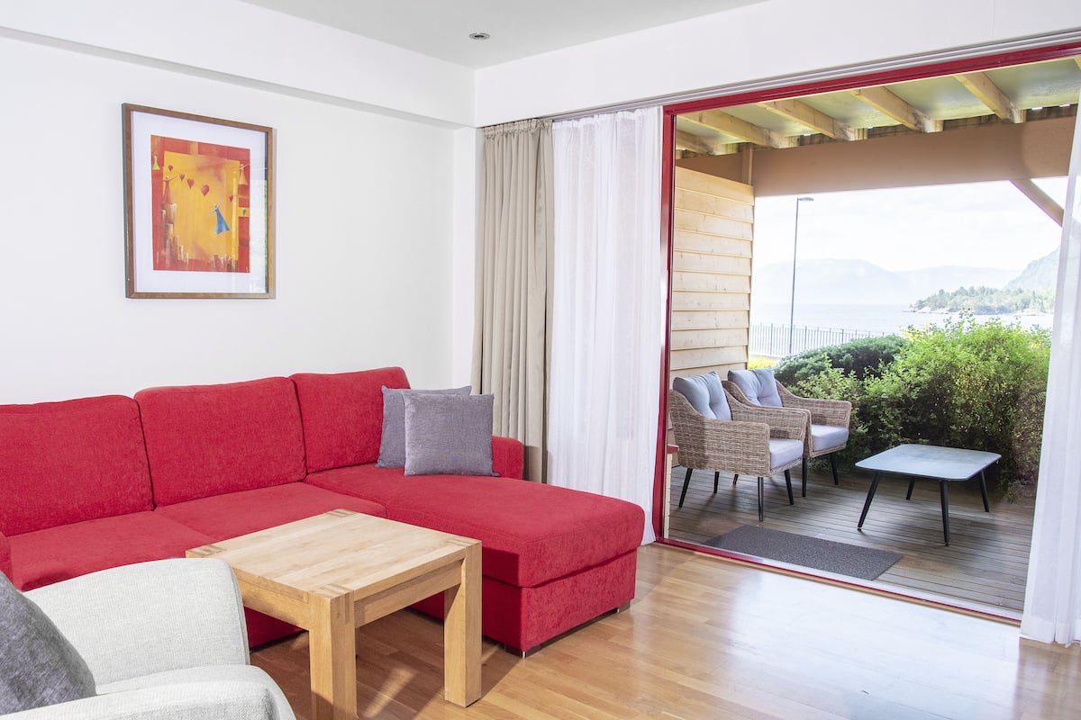 Un divano rosso componibile con un tavolino in legno, un quadro appeso al muro e vista all'aperto tramite una porta scorrevole in vetro.