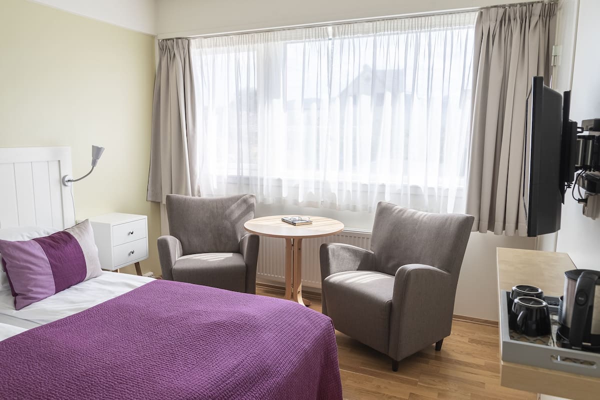 Una camera d'albergo con un letto, due poltrone, un tavolino rotondo, una televisione e una macchina per il caffè.