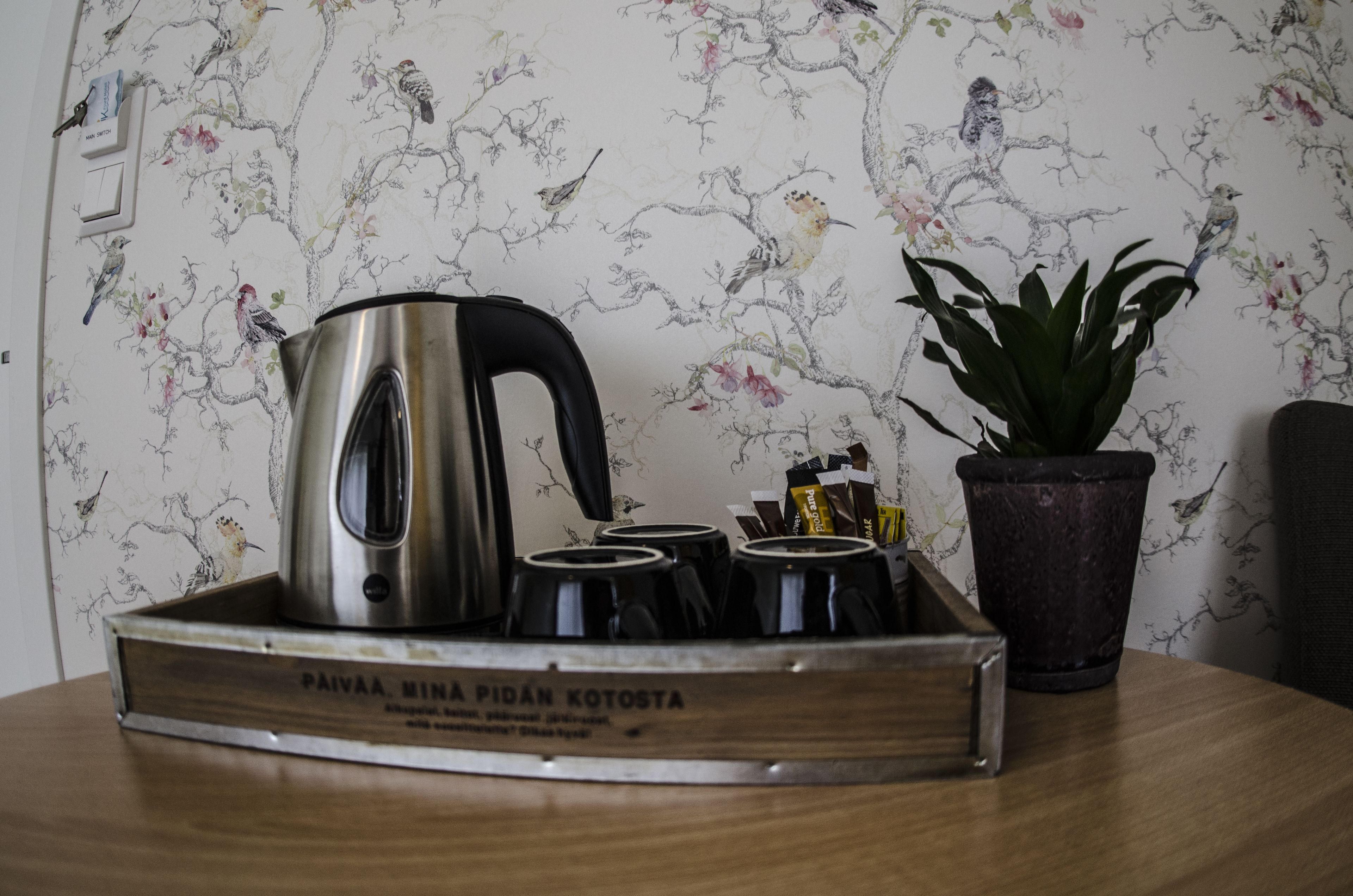 A tray with a stainless steel kettle and several black cups on a wooden table.