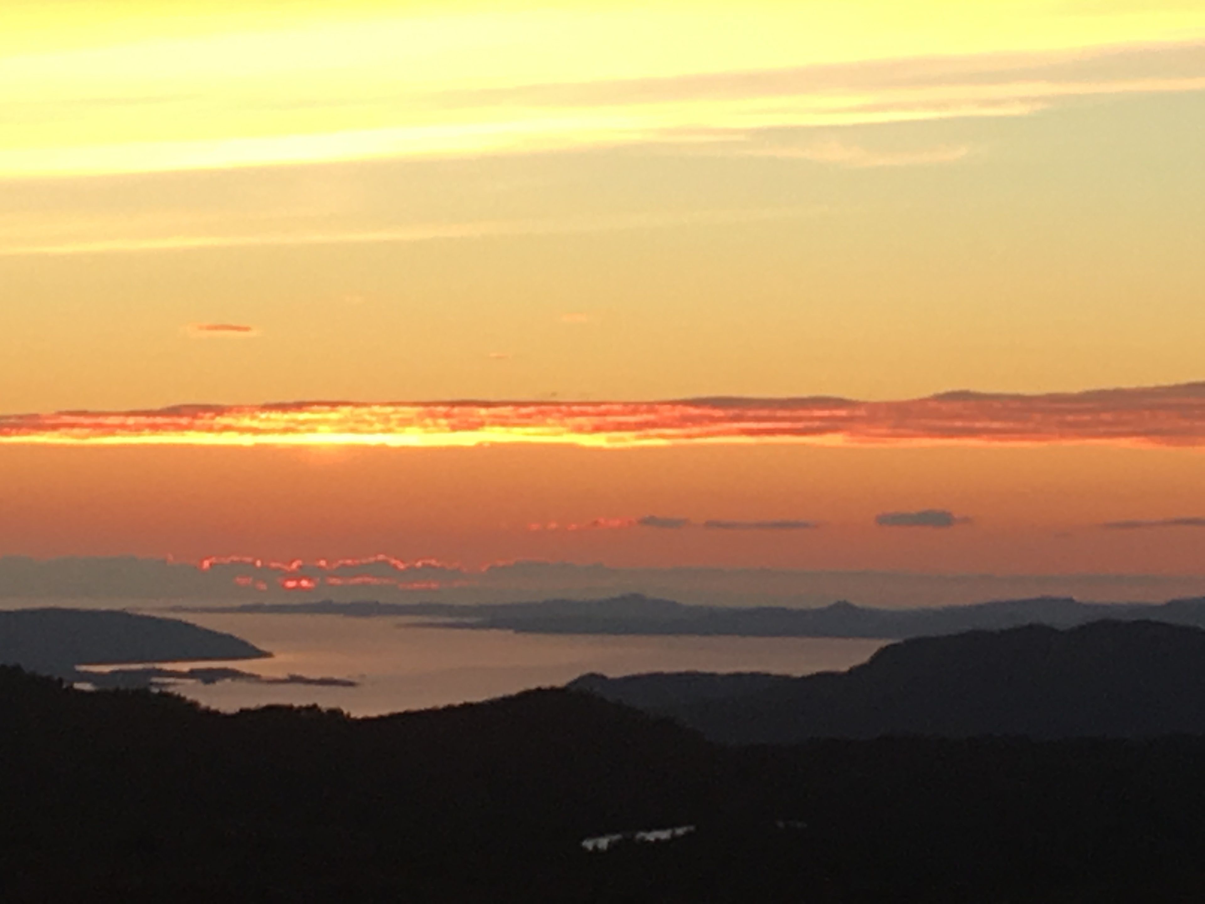 Un atardecer sobre un paisaje montañoso con una masa de agua al frente.