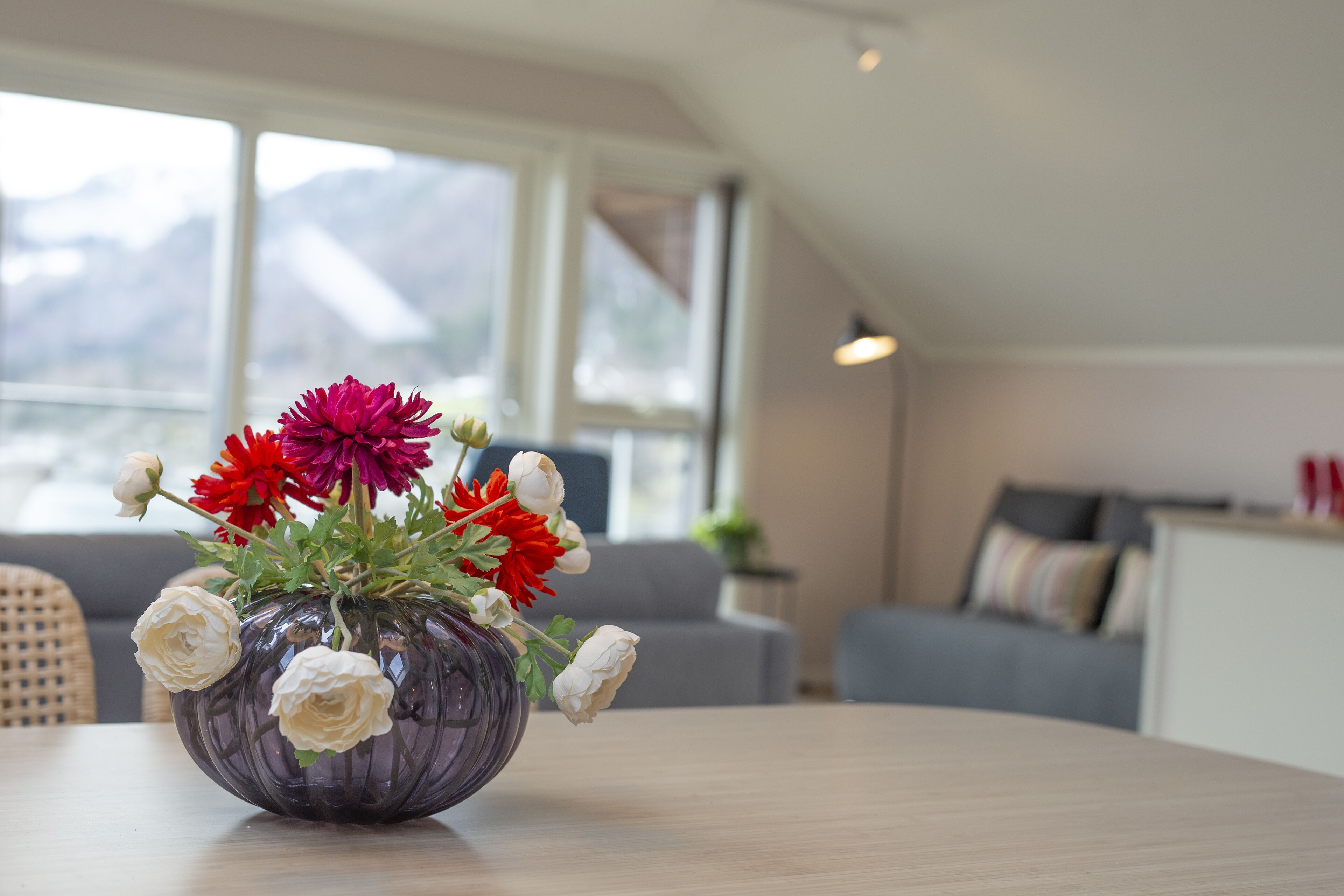 A room with a large window, a sofa, and a table with a vase of flowers.